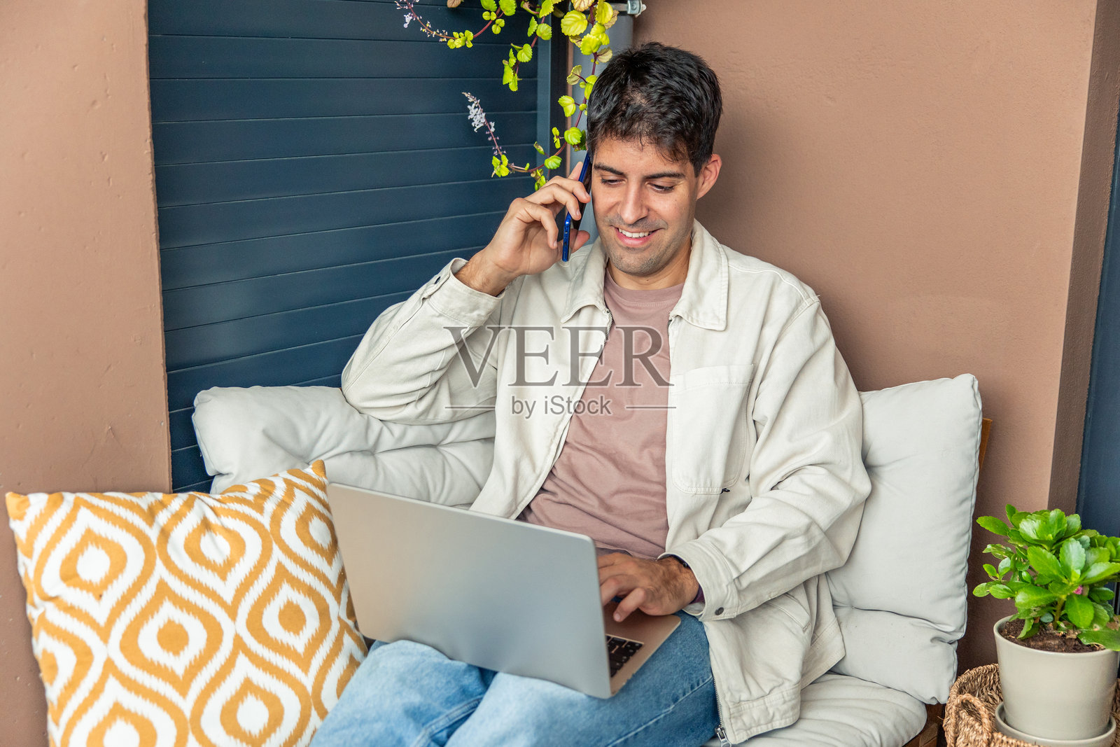 年轻的西班牙裔男性在家通过笔记本电脑和智能手机远程办公照片摄影图片