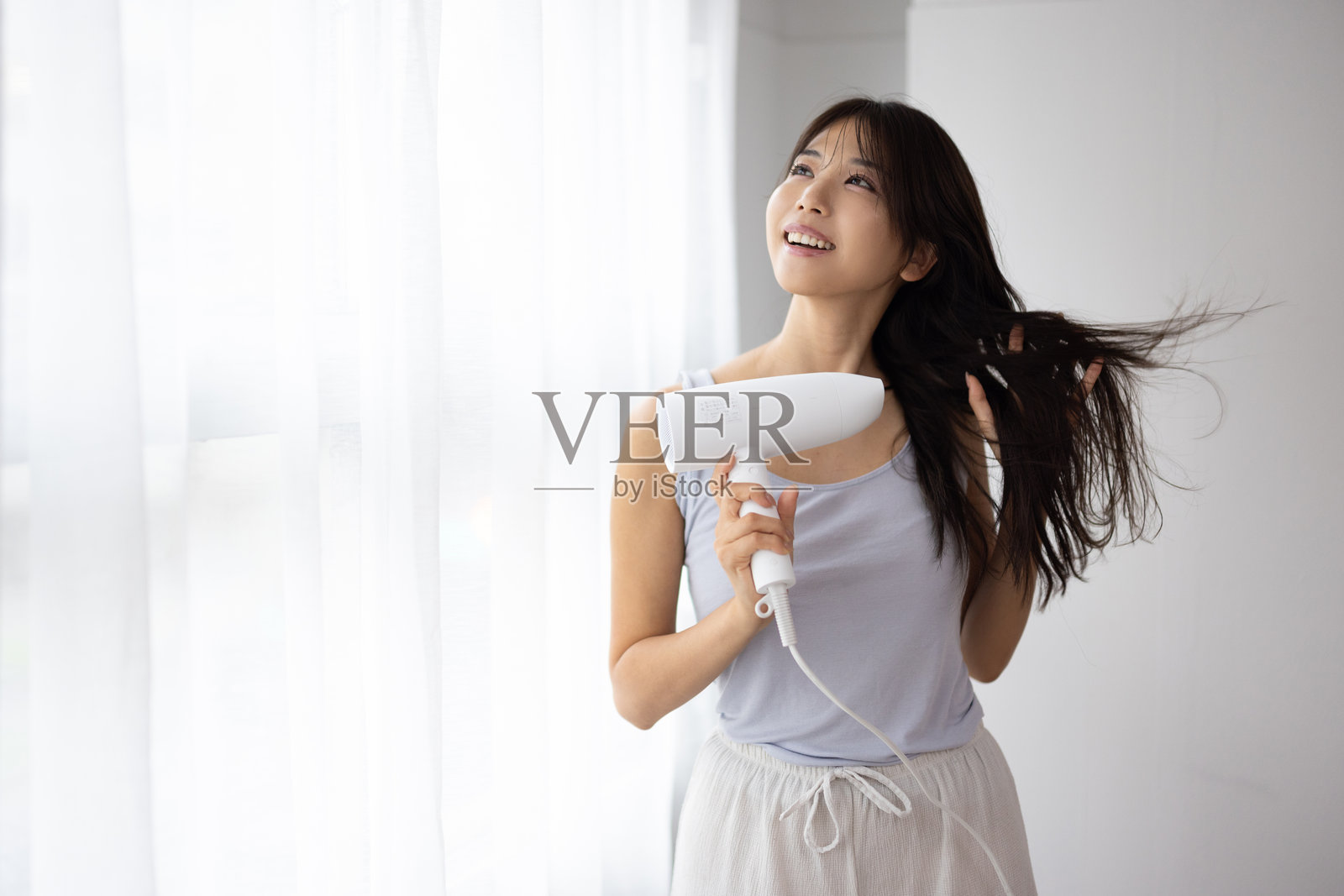 年轻女子在家中使用吹风机吹干头发照片摄影图片