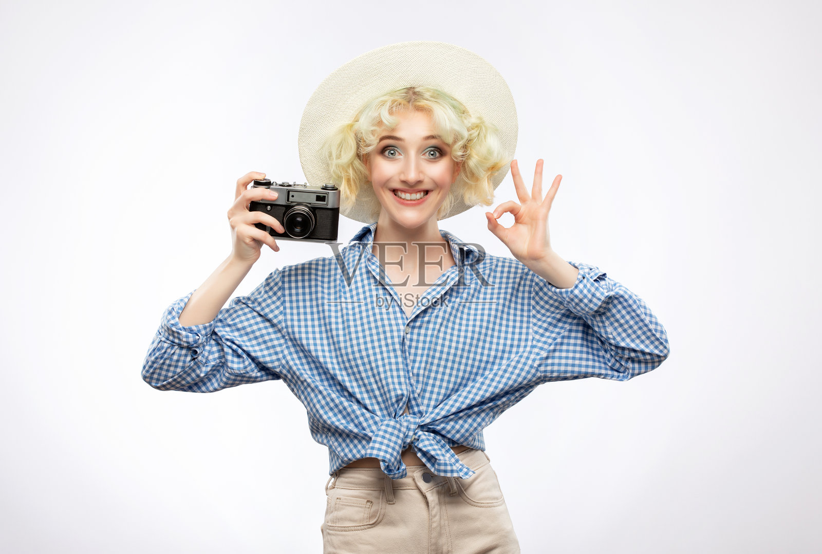 一位身穿蓝色格子衬衫、头戴草帽的美丽迷人女摄影师，手持一台复古相机，体现旅游出行概念。照片摄影图片