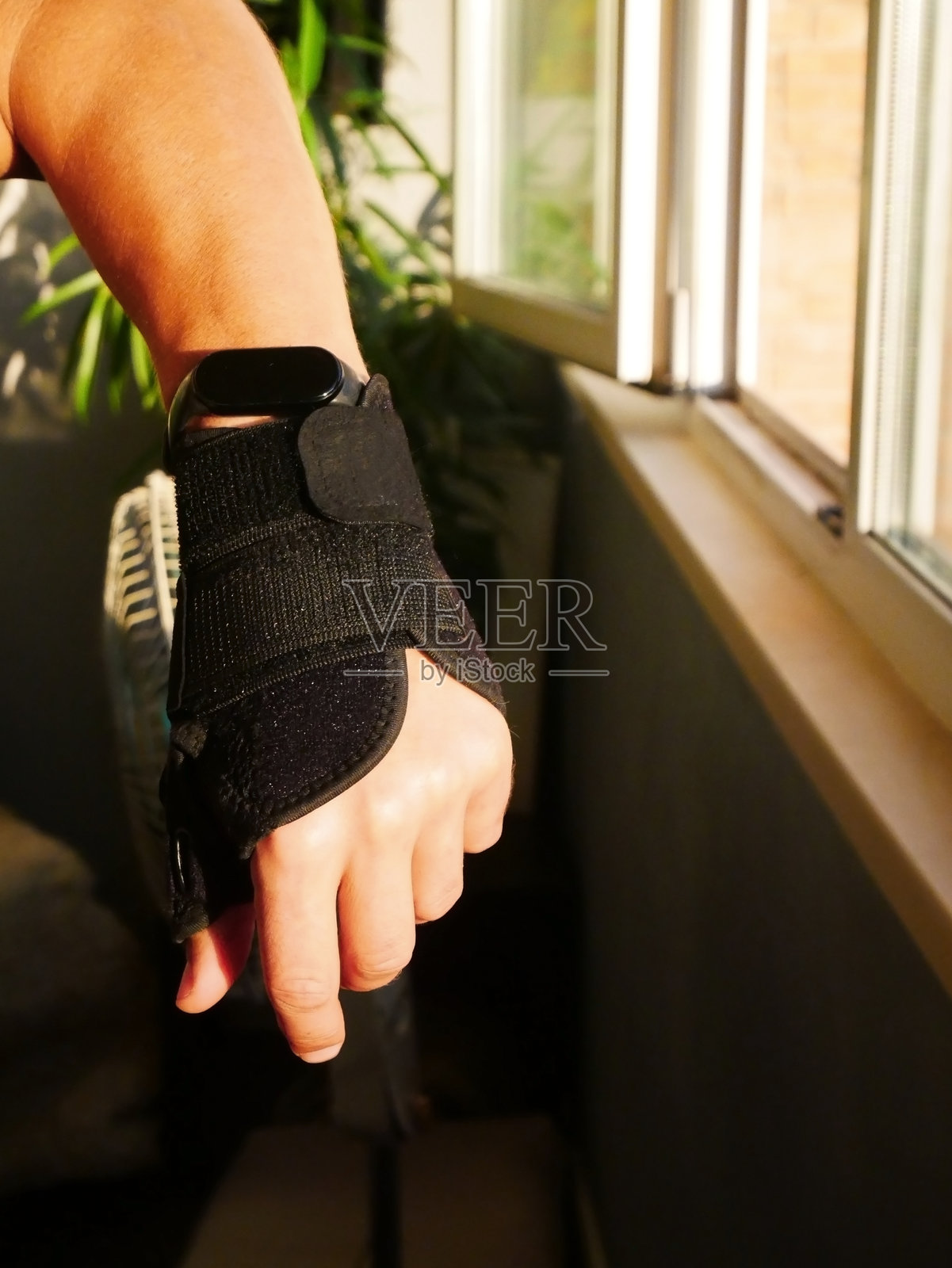 戴着护腕和智能手表的手，在阳光明媚的窗边照片摄影图片