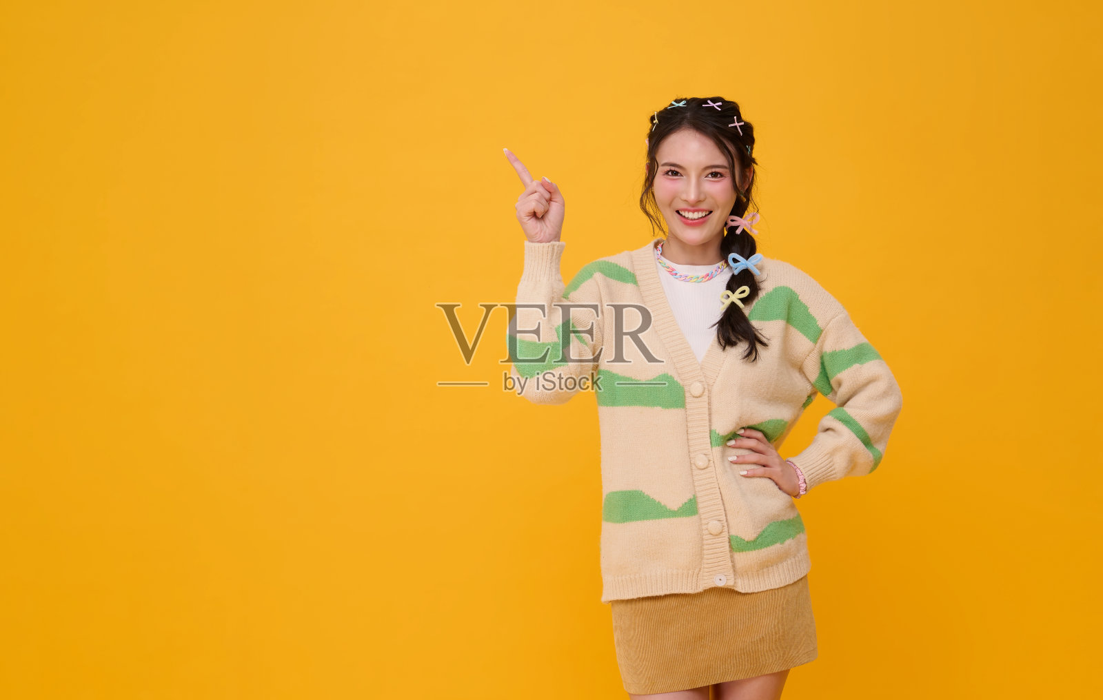 一位穿着休闲时尚服装的亚洲女性，面带微笑，手指指向一侧，表达着积极、自信、创意和现代生活方式，孤立在黄色复制空间背景上照片摄影图片