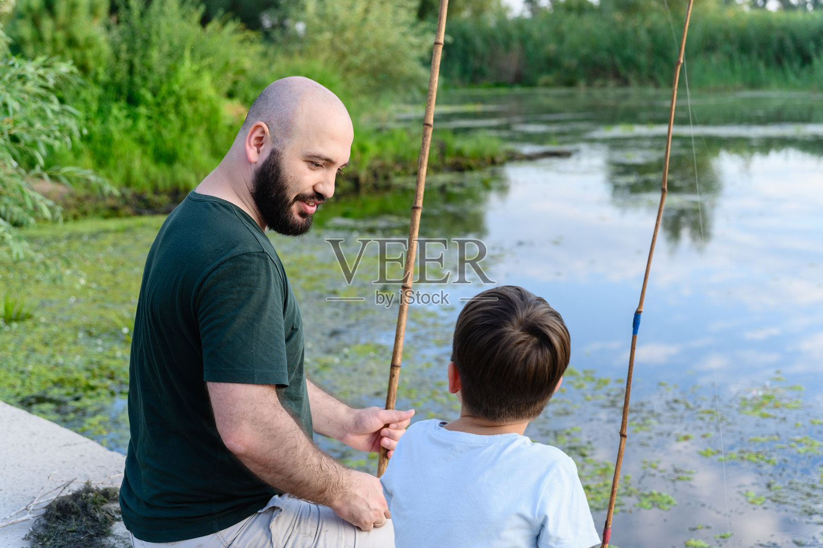 父亲和儿子在平静的河边一起钓鱼。照片摄影图片