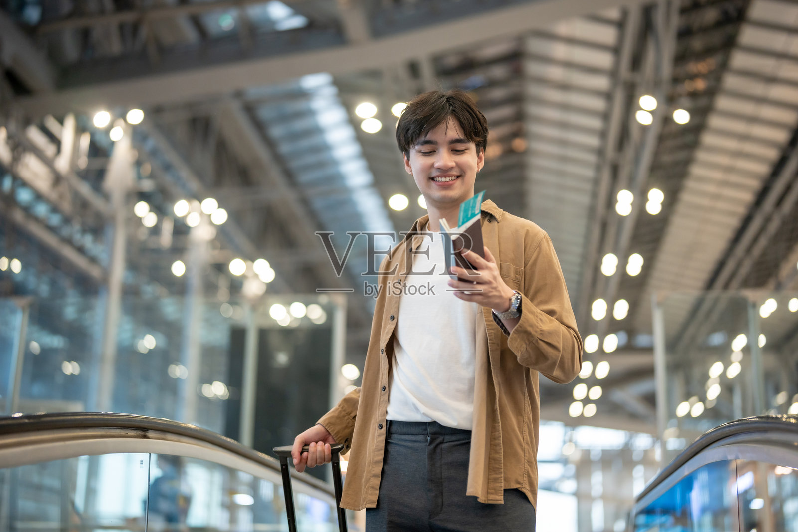 亚洲年轻男性乘客在机场航站楼走向登机口。英俊有魅力的男性游客因独自一人搭乘飞机出国旅行度假而感到开心和兴奋。照片摄影图片