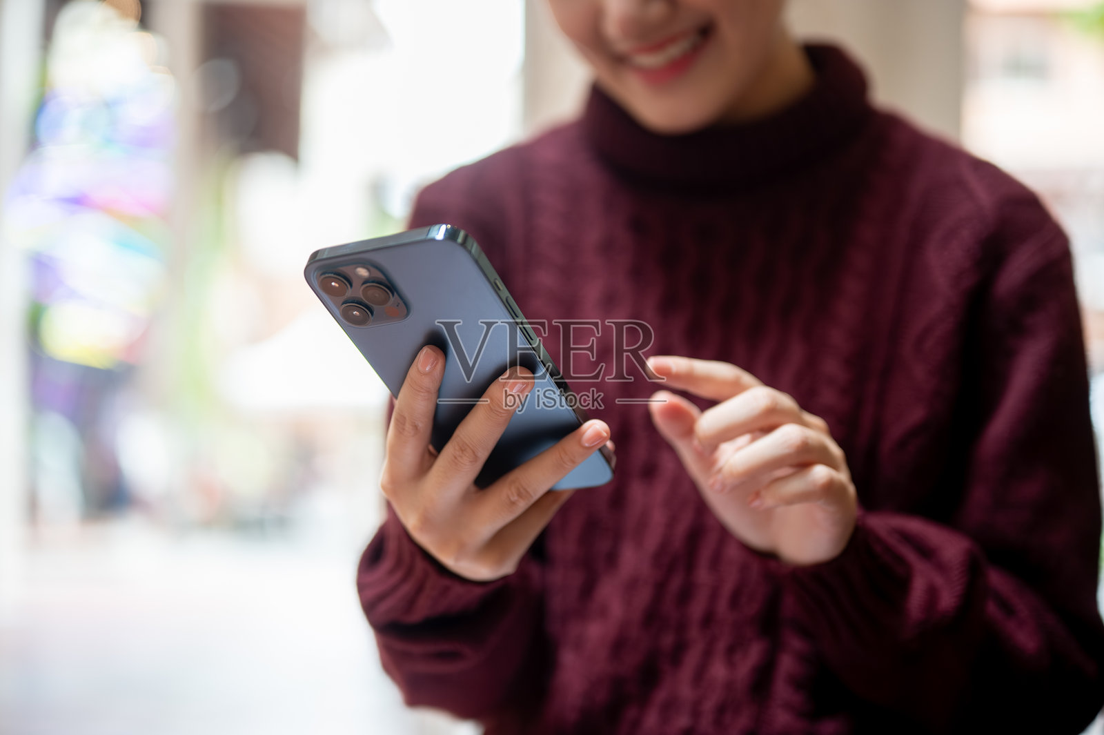 特写：一名女性的手指着手机，她正坐着或站着身处一栋建筑内。照片摄影图片