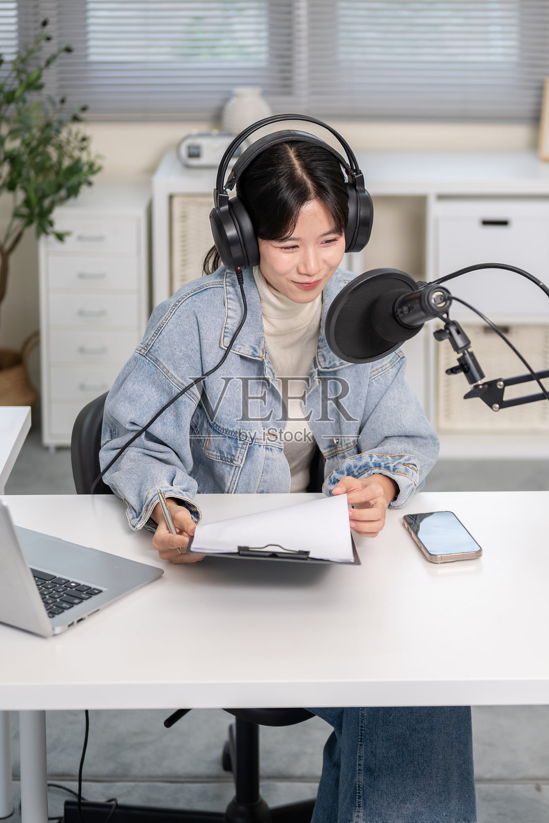 亚洲女性戴着麦克风耳机，在家中或工作室里使用笔记本电脑进行广播或播客录制照片摄影图片