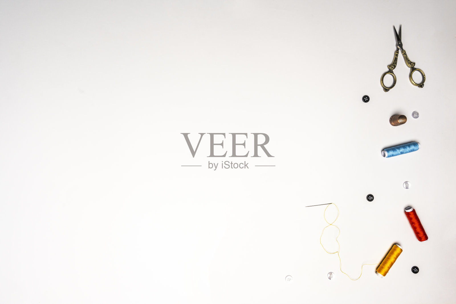 白色背景上的彩色线轴，配有穿好线的针、金色剪刀和顶针照片摄影图片