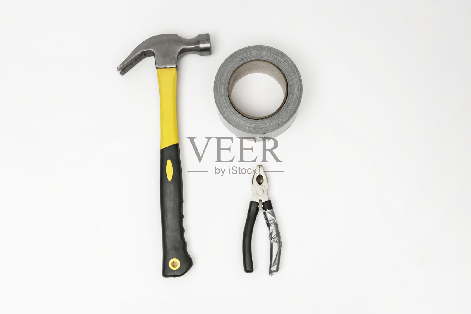 白色表面上的一把钳子、一卷灰色胶带和一把木工锤照片摄影图片