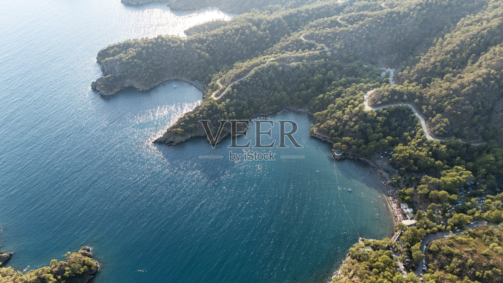 无人机航拍视角，俯瞰被葱郁松林环绕的僻静绿松石色海湾照片摄影图片