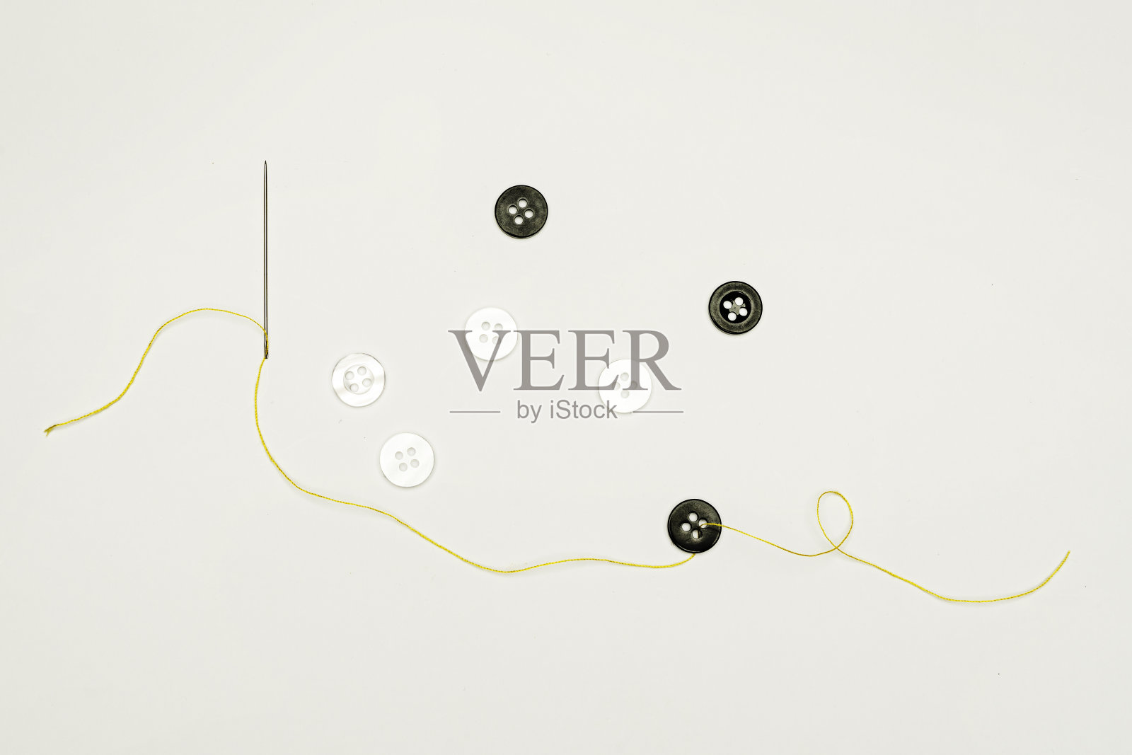 一根针，穿过黑色纽扣，线是黄色的照片摄影图片