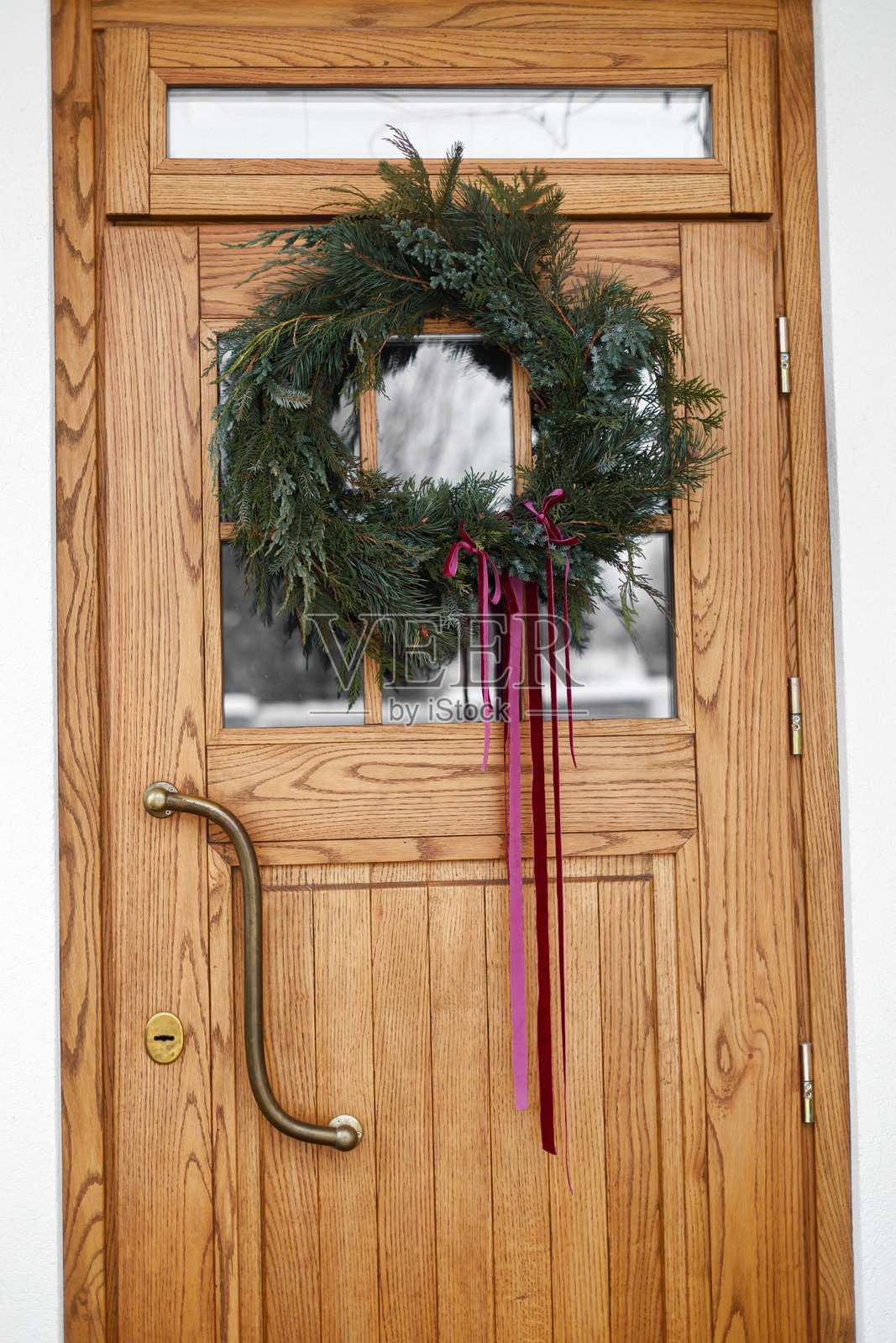 风格化的圣诞花环，饰有红色丝带，悬挂在木门上。冬季农舍前门的精美节日装饰，留有复制空间。圣诞快乐照片摄影图片