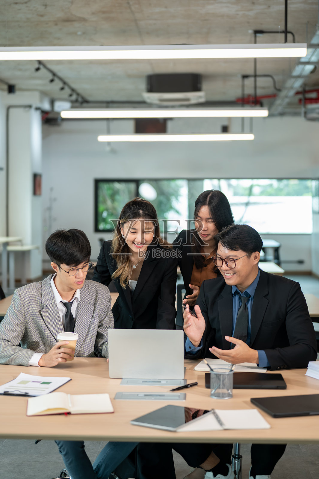 一位面带微笑的女商人正在会议室的木桌旁，看着笔记本电脑，与同事交谈或解释。照片摄影图片
