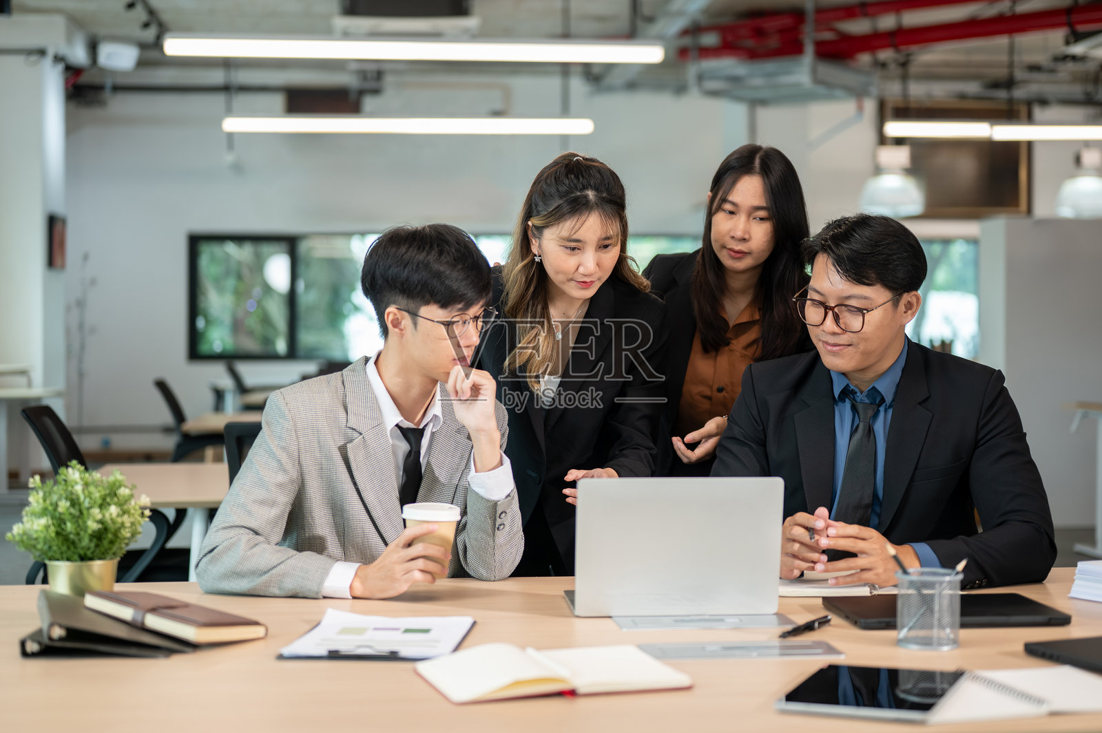 一位女商人在会议室的木桌旁，一边看着笔记本电脑，一边向同事解释着。照片摄影图片