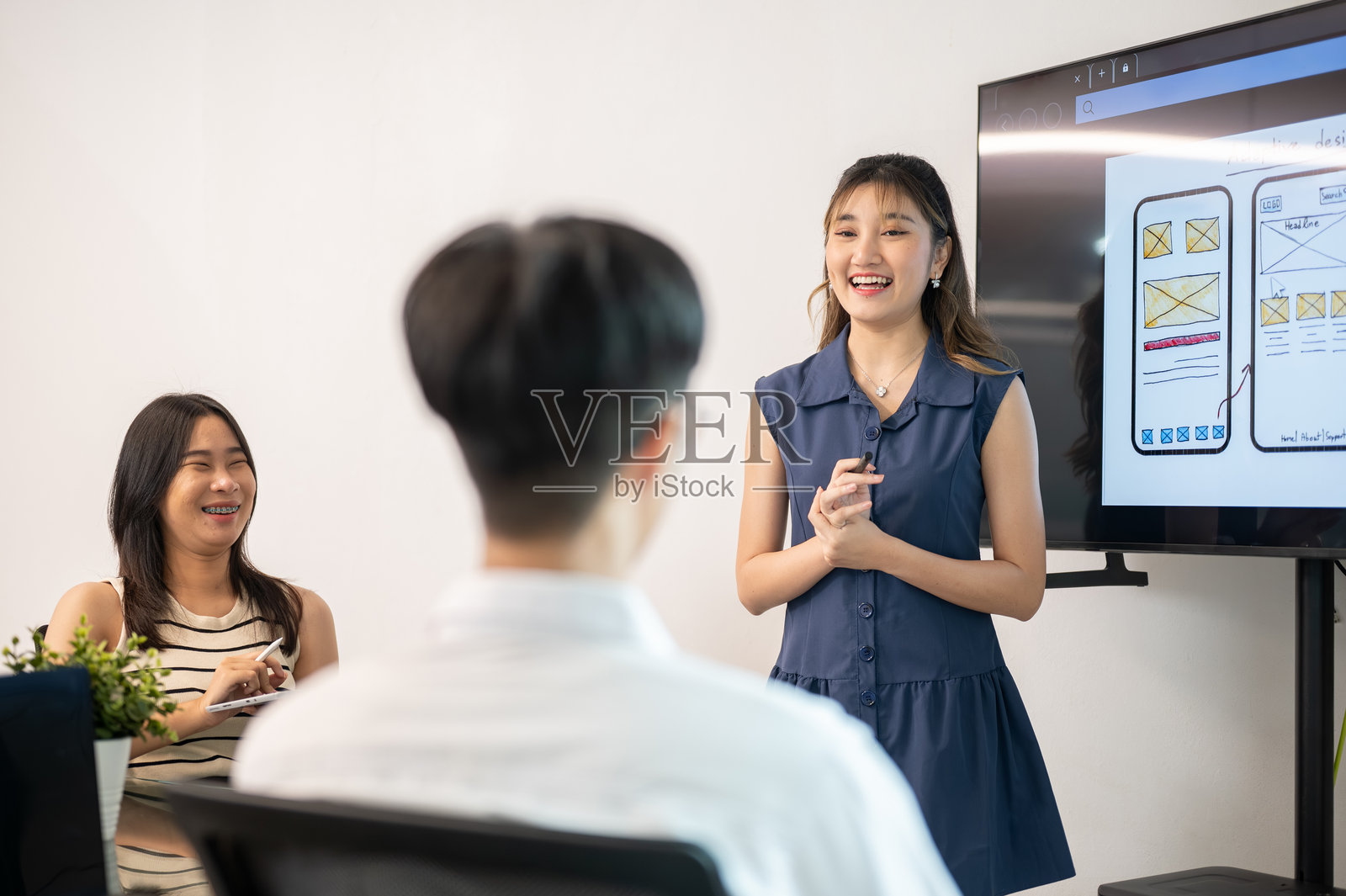 一位亚洲女性站在显示器前，在办公室会议中向同事展示移动应用设计照片摄影图片