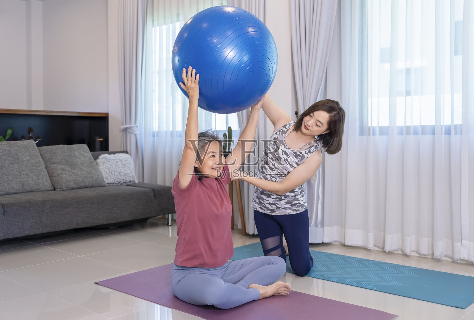 穿着运动服的亚洲老年女性在私人教练的指导下使用瑜伽球锻炼照片摄影图片