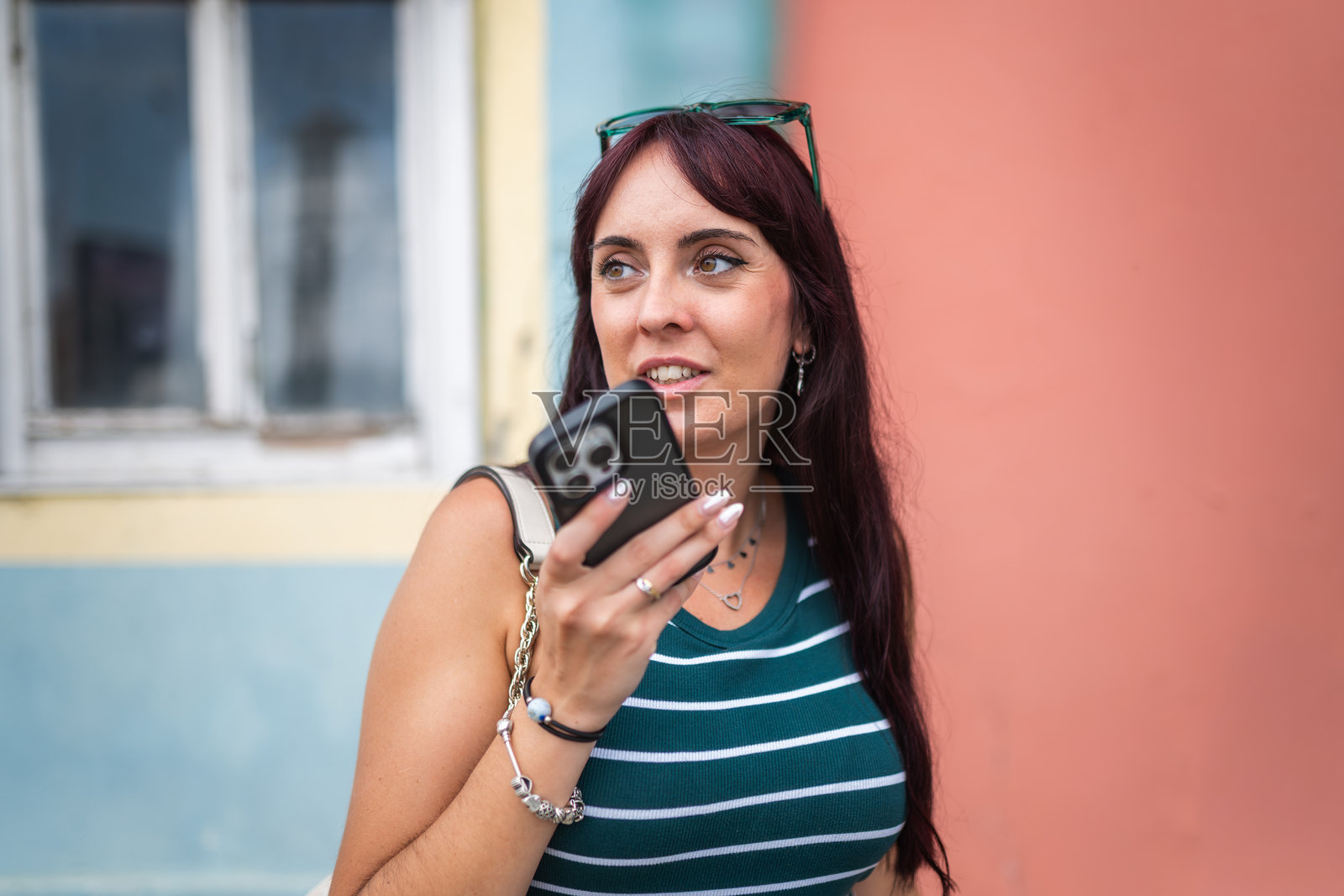 女性在城市背景下通过智能手机发送语音消息，背景色彩鲜艳照片摄影图片
