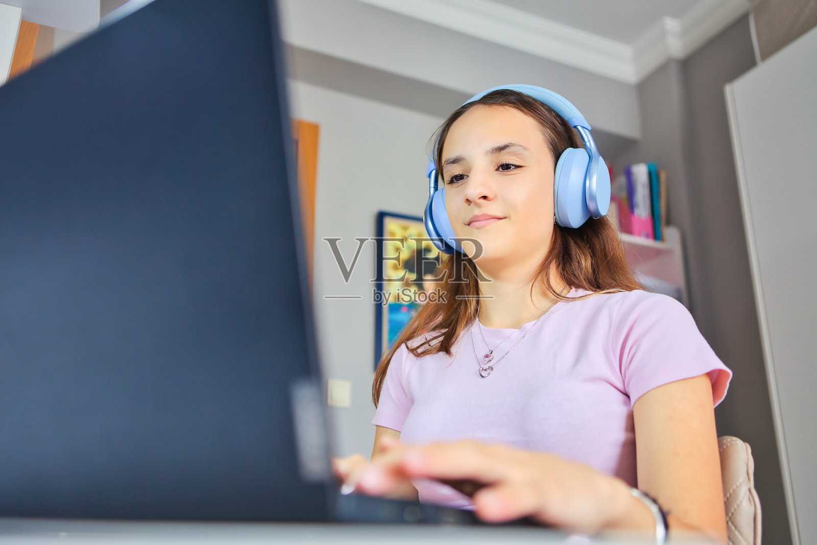 一名戴着耳机的美丽女孩在房间里使用笔记本电脑的特写。照片摄影图片