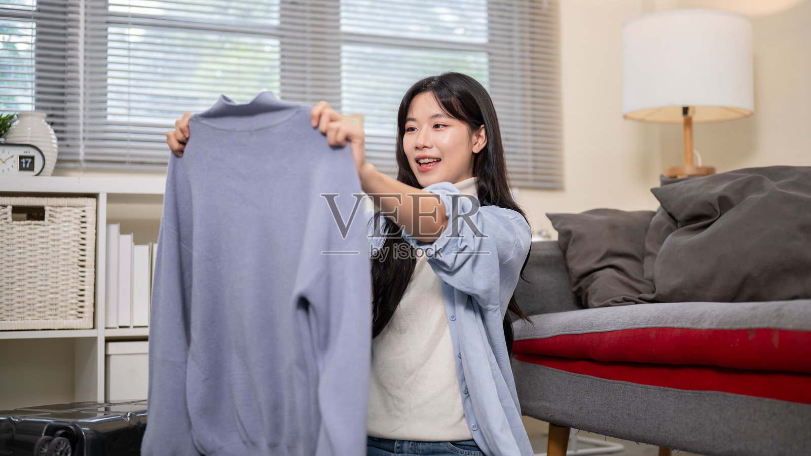 一位女士微笑着，在卧室或客厅里整理行李，准备出行，她手中拿着一块布。照片摄影图片