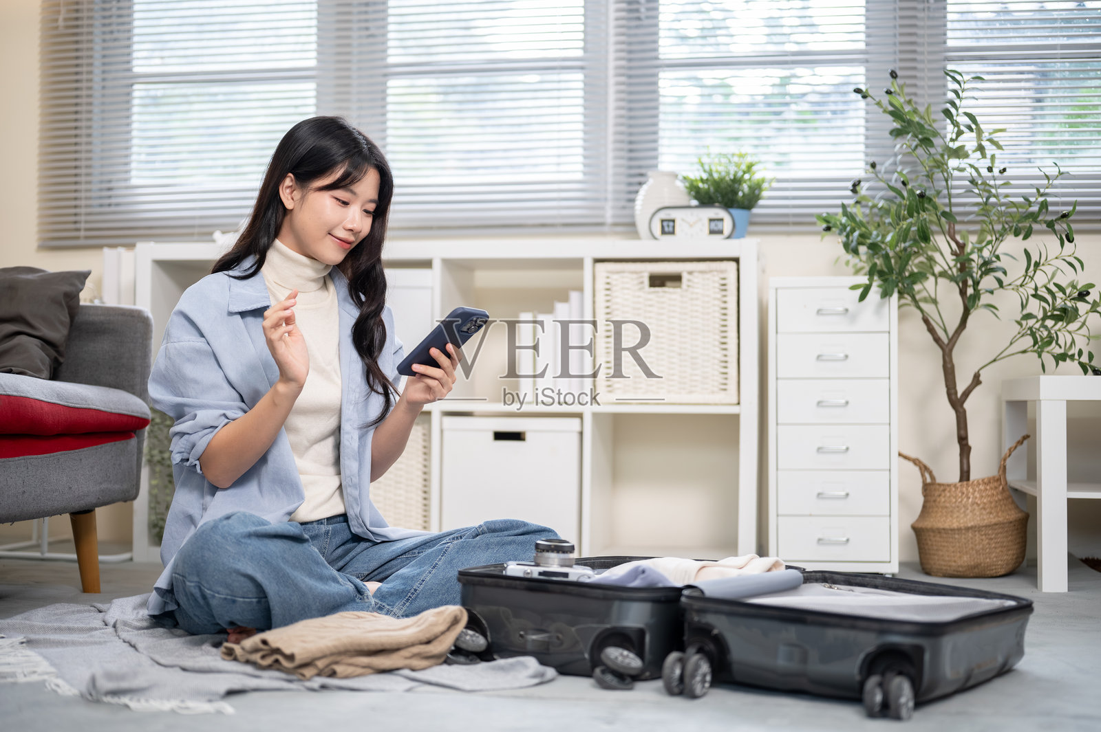 亚洲女性在卧室或客厅地板上整理或打包行李，同时看着手机照片摄影图片