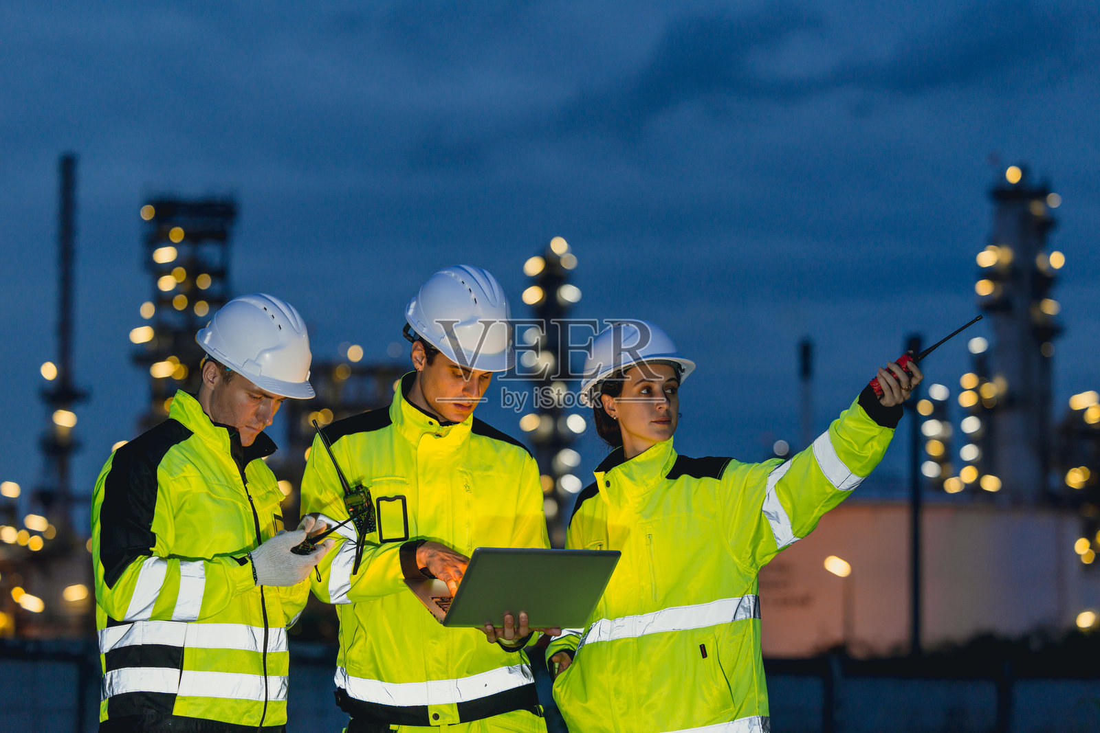 工程师团队在石油和天然气炼油厂服务中心进行夜班工作，工人们在夜晚的石油工业工厂背景下辛勤工作。照片摄影图片