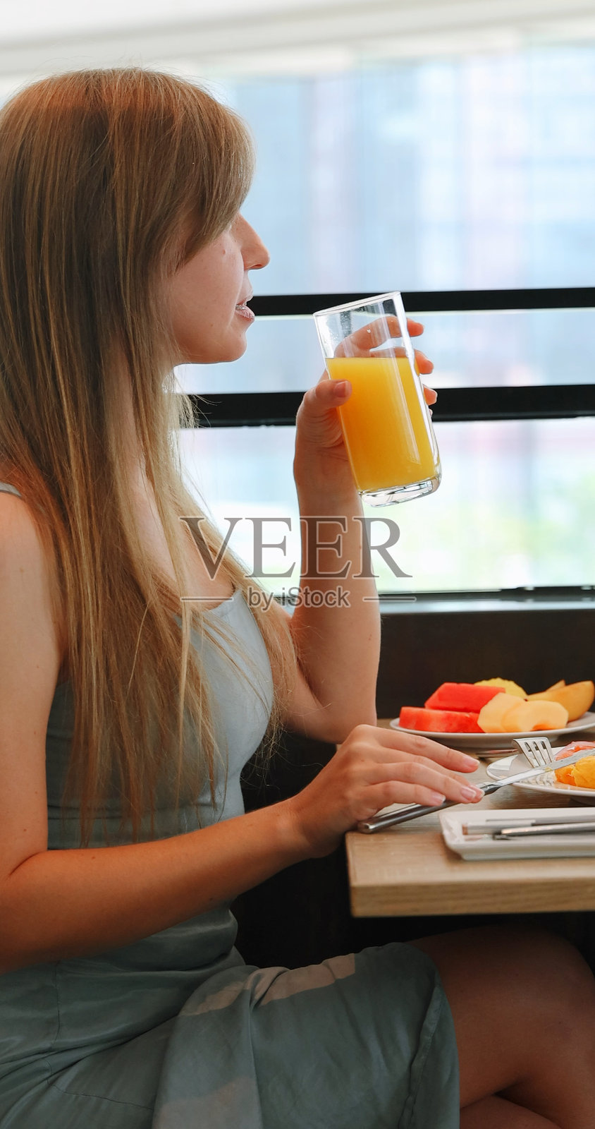 女子在餐桌旁享用早餐，搭配橙汁和水果，背景为城市景观照片摄影图片