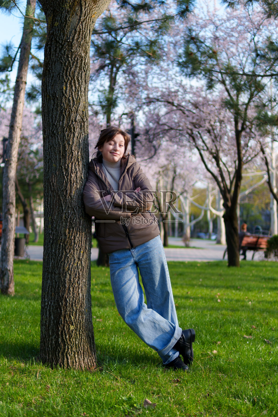 春日公园里一位少女的肖像，她倚靠着一棵树站立照片摄影图片