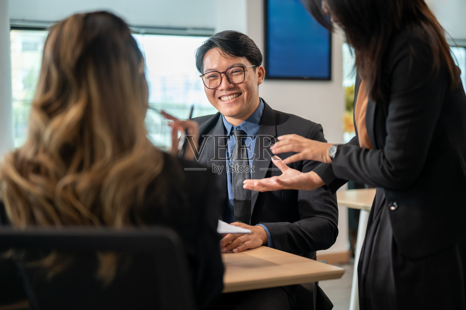 一位女商人和一位微笑着的男士在办公室的木桌旁，背对着镜头，倾听同事的谈话。照片摄影图片