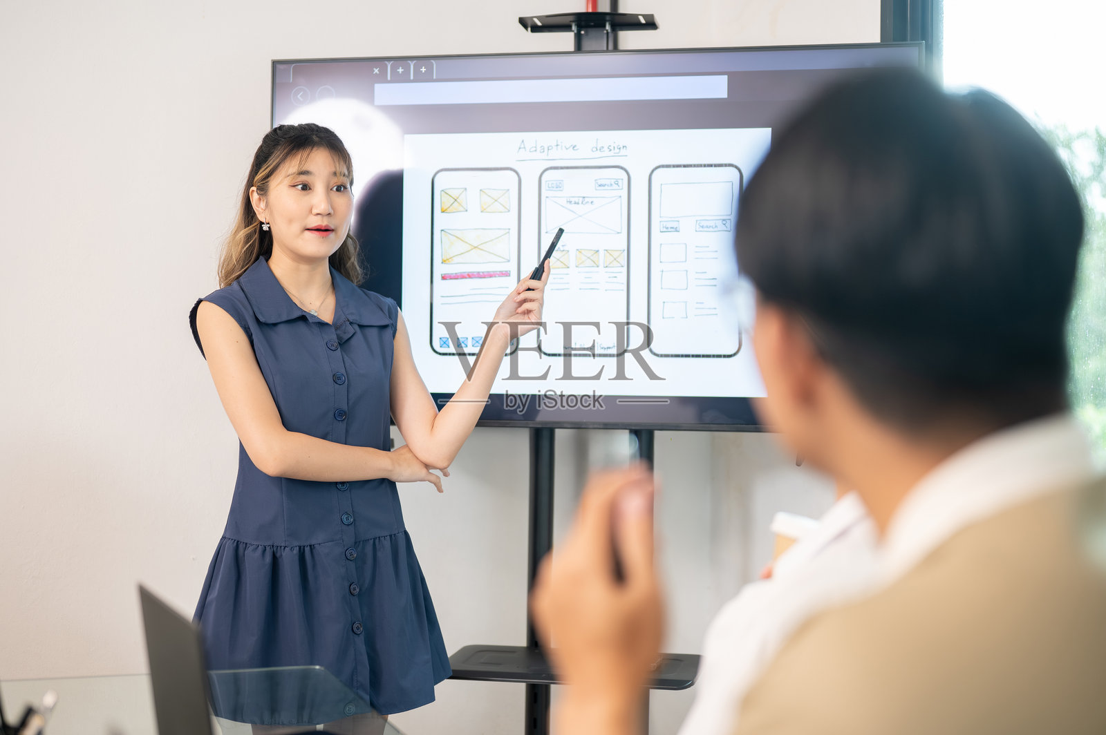 一位亚洲女性在办公室会议中，用笔指向显示器上的移动应用设计，向同事们展示。照片摄影图片