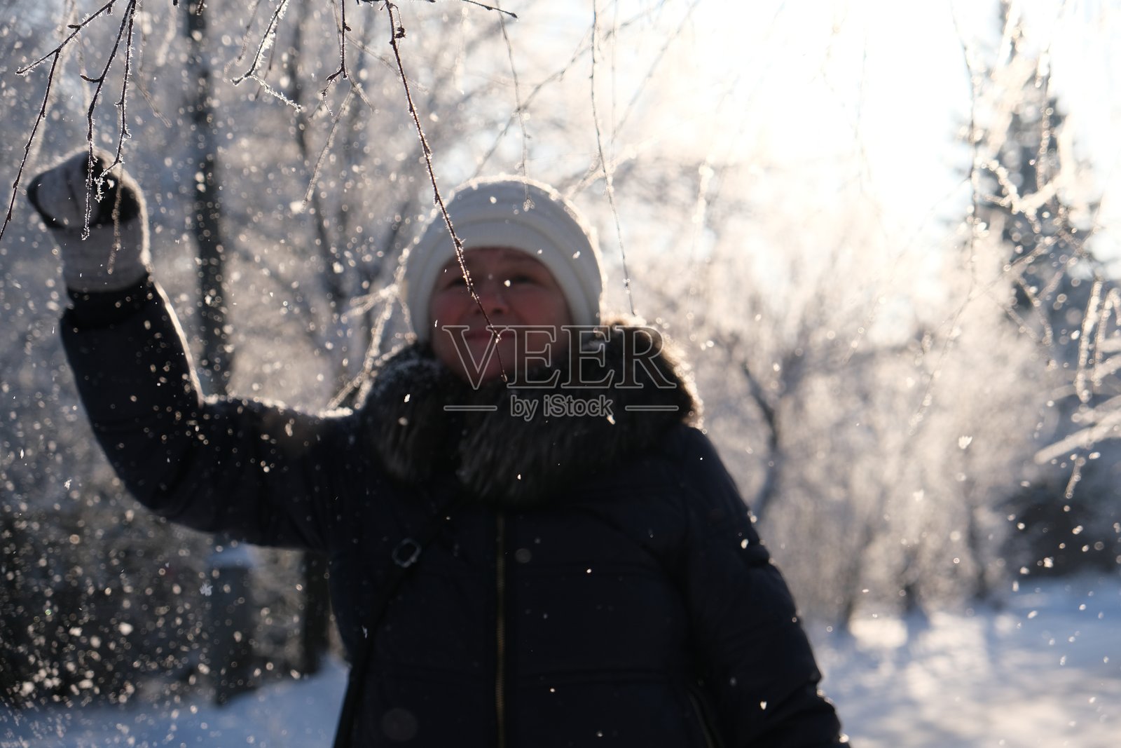 下雪的街道上，一位戴着白色帽子、穿着蓝色羽绒服的女士。一位沉思迷人的中年女性，带着宁静的微笑。阳光明媚的户外冬季假期。深呼吸感受清新。照片摄影图片