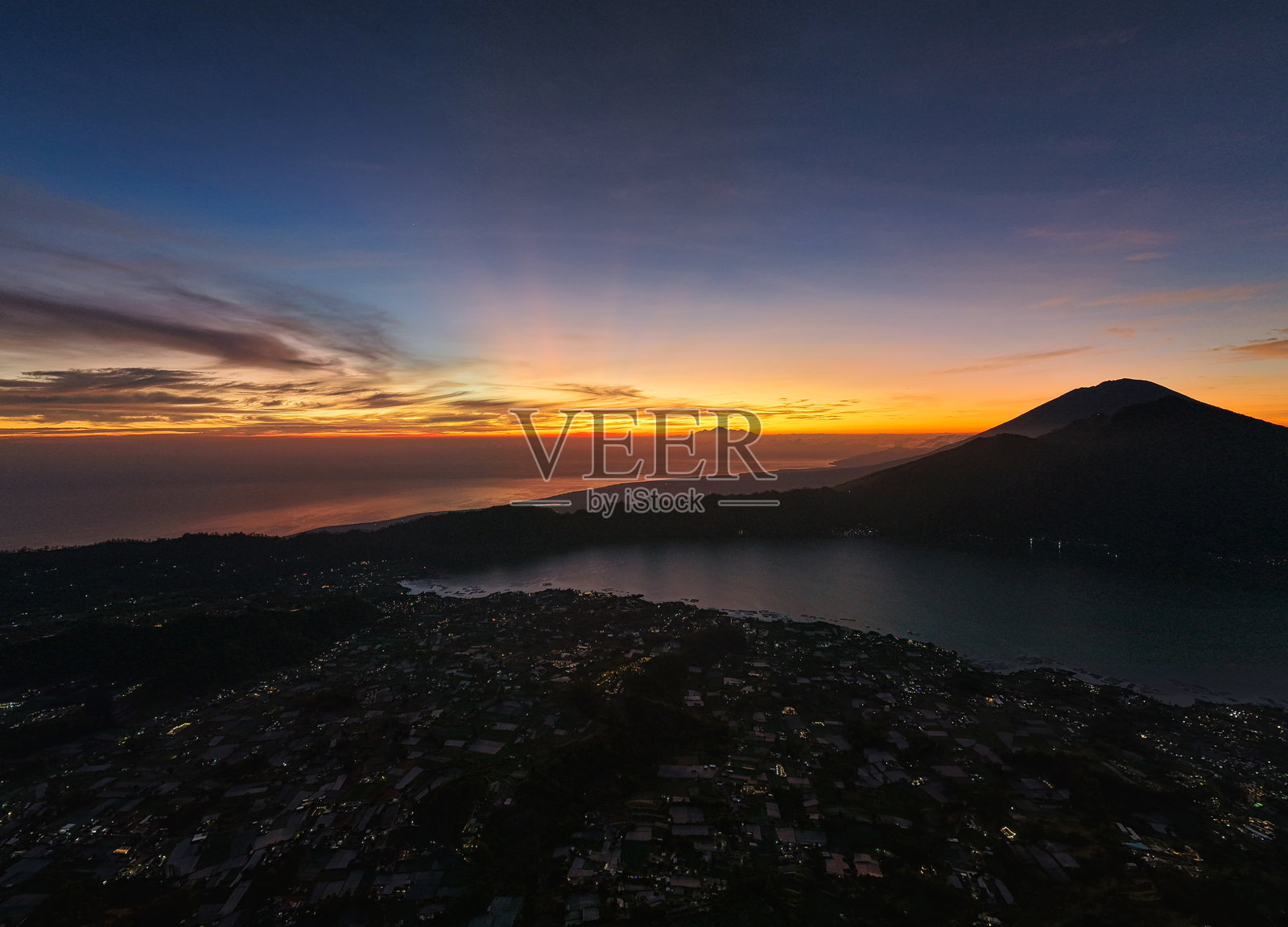 宁静的日落，火山湖泊，闪烁的村庄灯光，倒映在水中，位于巴厘岛金塔马尼的阿邦阿贡照片摄影图片