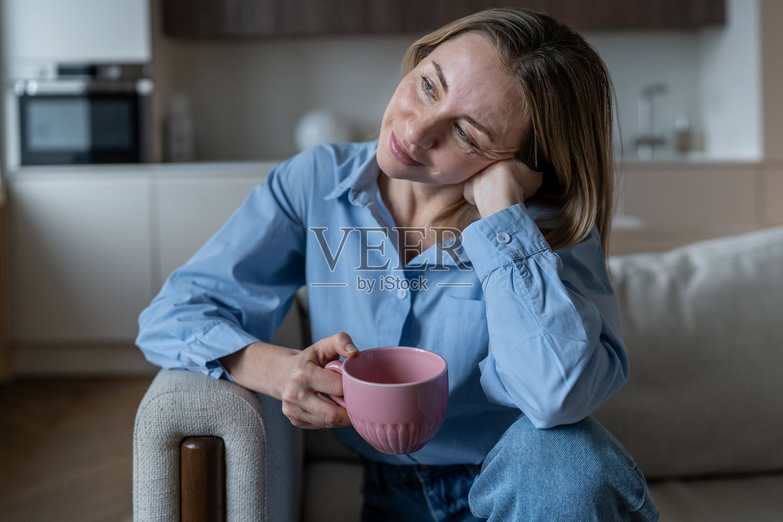 一位宁静的中年女性在家里的沙发上享受咖啡时光，心中充满对生活的美好遐想。照片摄影图片