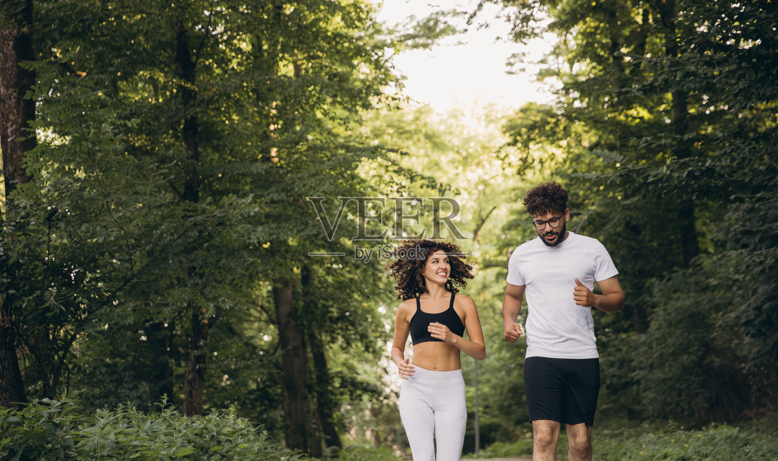 年轻的多民族情侣在森林里跑步照片摄影图片