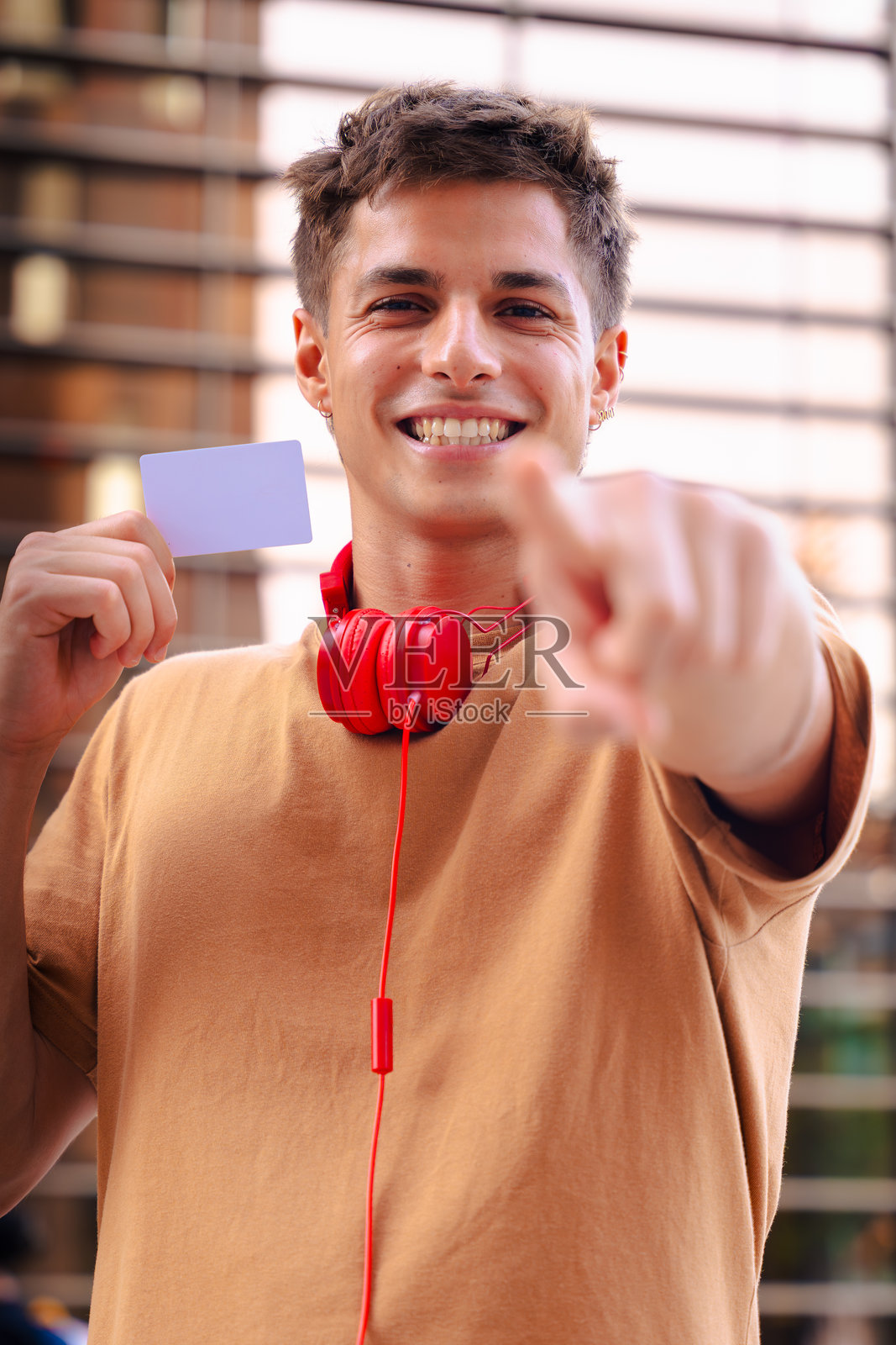 面带微笑的年轻男子在户外手持空白卡片面向镜头，他戴着红色耳机。照片摄影图片
