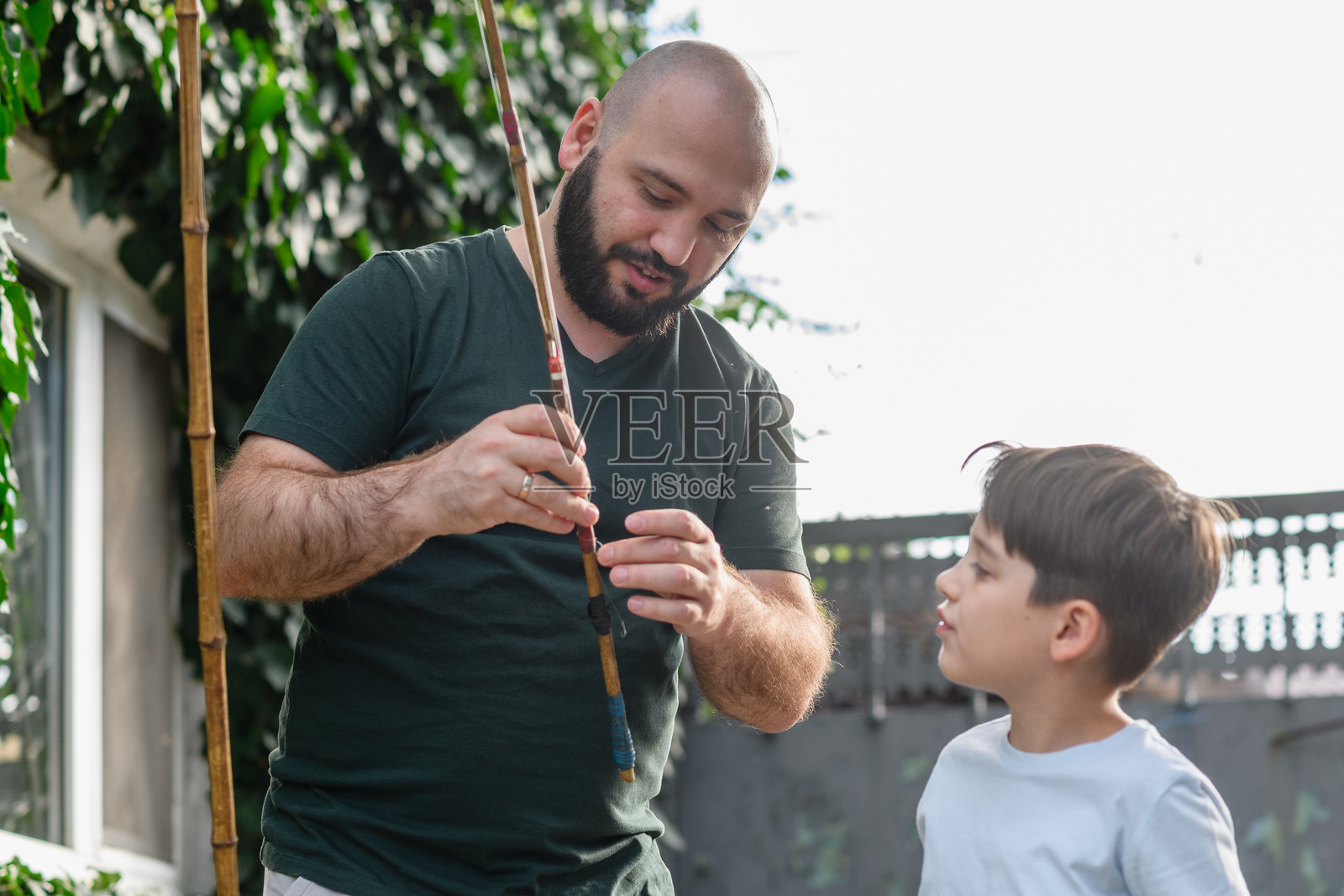 父亲在户外教儿子组装鱼竿。照片摄影图片