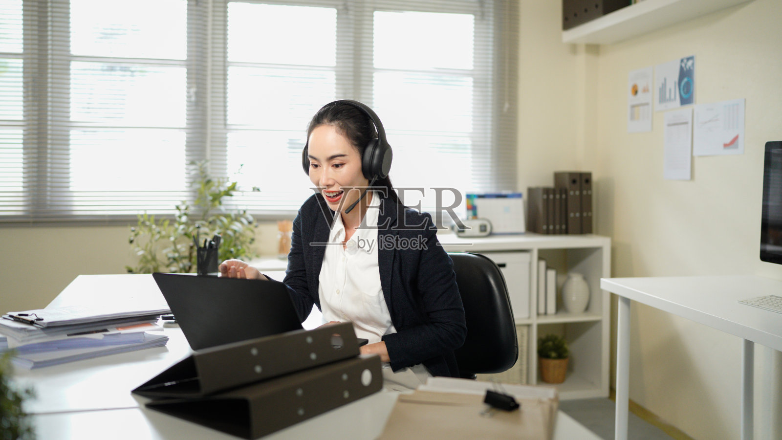 商务女性，呼叫中心顾问，使用笔记本电脑提供客户服务、支持或咨询，在办公室工作。专业的亚洲顾问或佩戴耳机的快乐客服代表，用于联系我们或电子商务。照片摄影图片