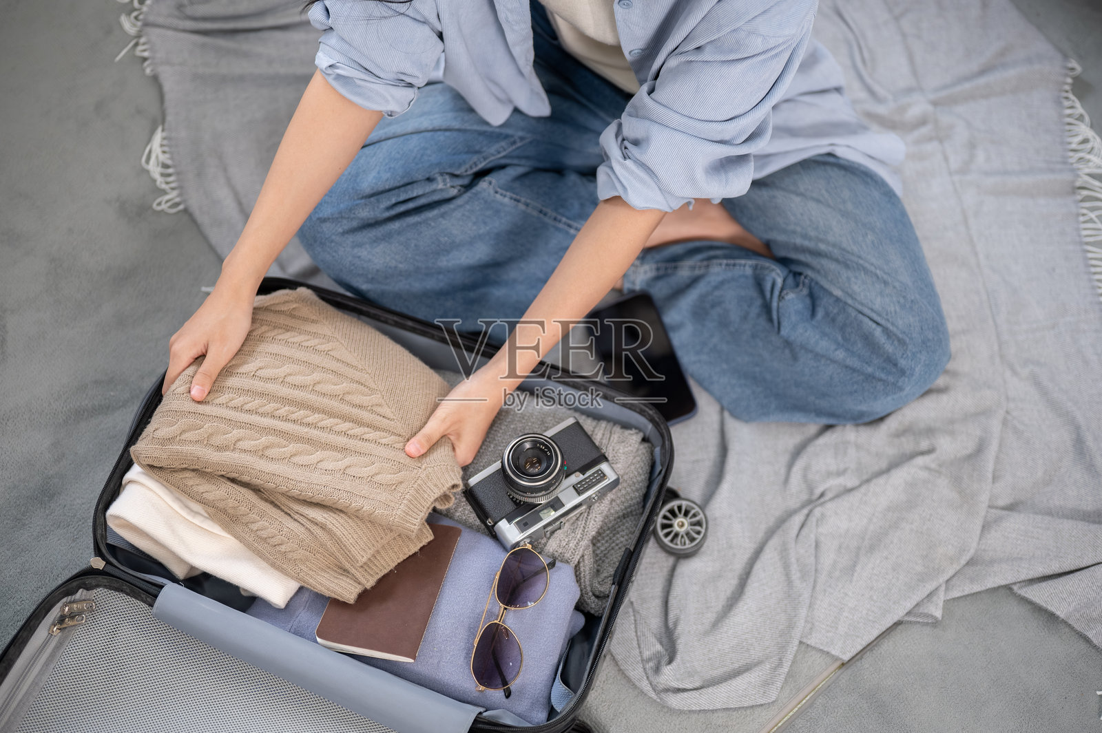 俯视女子在地板上整理行李，将折叠的衣物放到一边，旁边放着相机。照片摄影图片