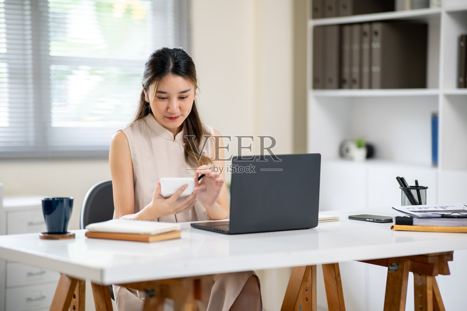 漂亮的亚洲女职员在办公室的白桌上，笔记本电脑旁边拿着并使用计算器照片摄影图片