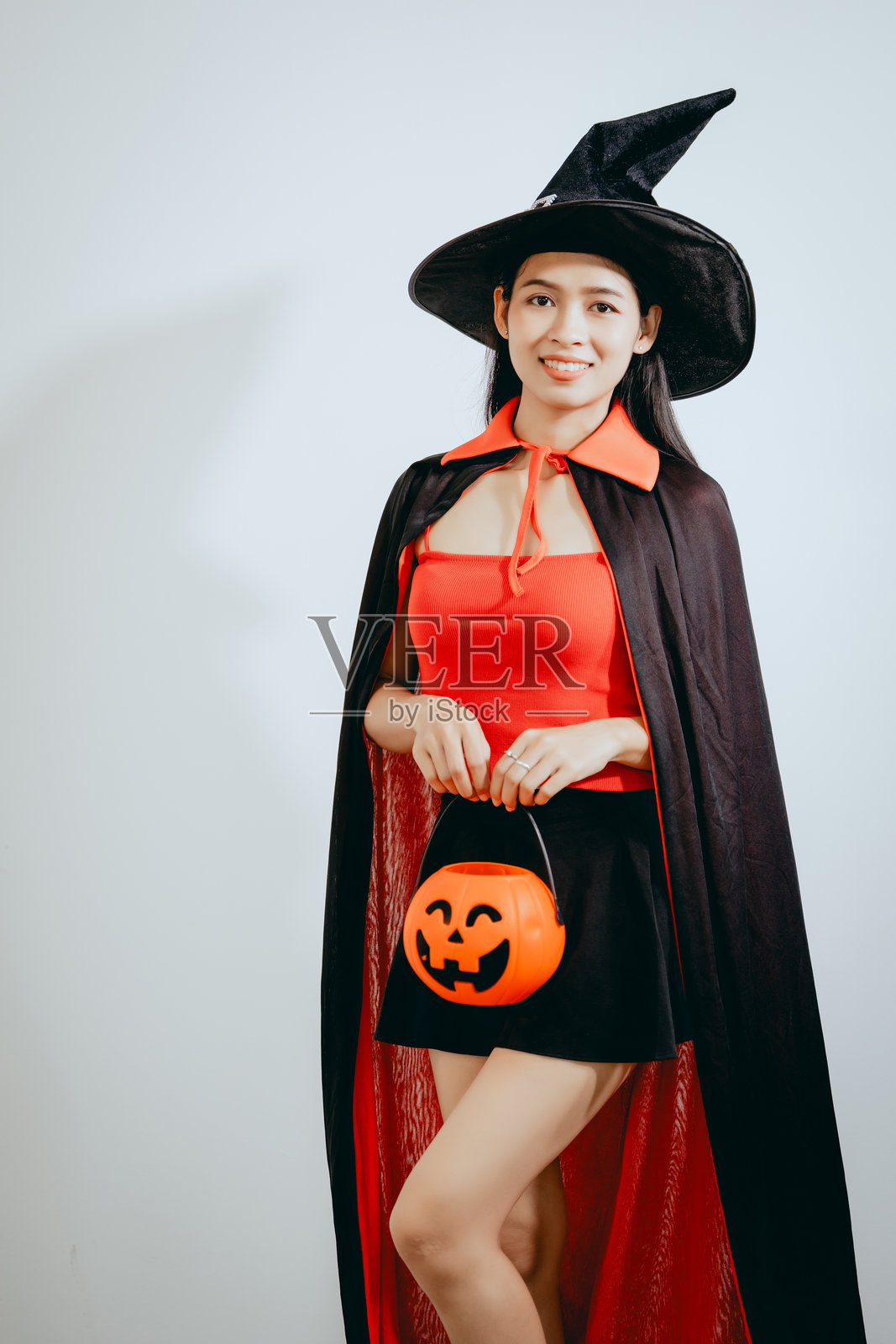 一位身穿巫女服饰的美丽年轻亚洲女性，手持橙色南瓜，在干净的白色背景前欢庆万圣节，散发出节日的精神、快乐和俏皮的节日魅力。照片摄影图片