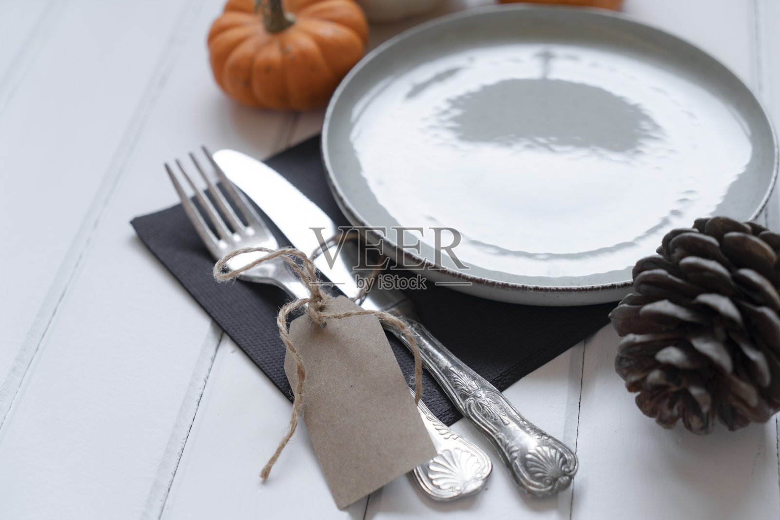 一张快乐感恩节标签挂在一个小南瓜和盘子上，餐具摆放在桌上照片摄影图片