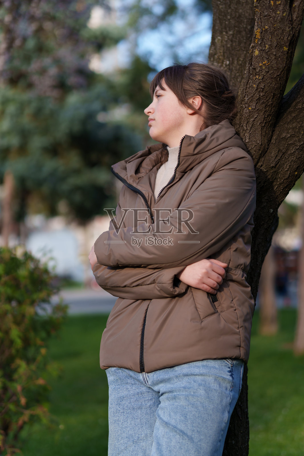 一名少女在春日公园里，倚靠着树站立的肖像照照片摄影图片