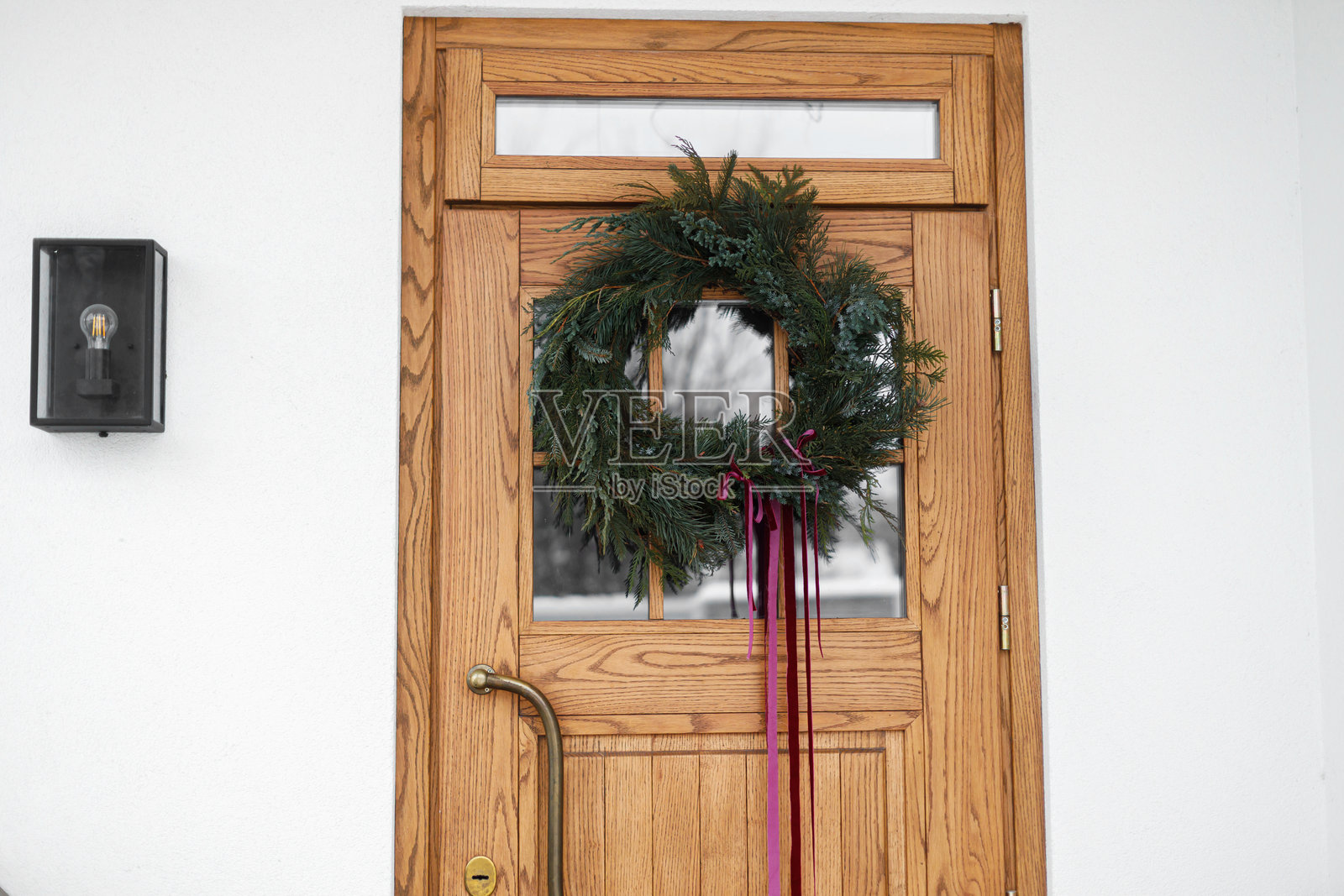 时尚的圣诞花环，系着红丝带，挂在木制前门上。现代农舍外墙的冬季节日装饰，可复制空间。圣诞快乐照片摄影图片