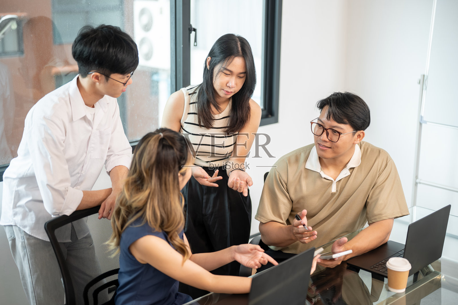 亚洲男子在办公室的玻璃顶会议桌旁，手持手机向同事们解释或讨论照片摄影图片