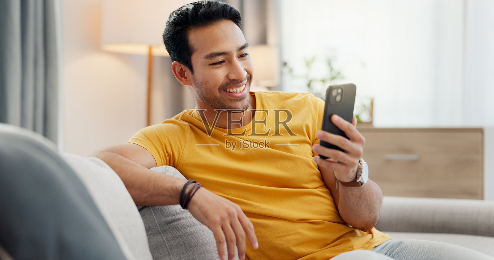 一个男人坐在沙发上，通过手机进行视频通话，进行社交网络和在线聊天，享受周末的放松时光。他正通过手机应用程序进行沟通、上网和交谈。照片摄影图片