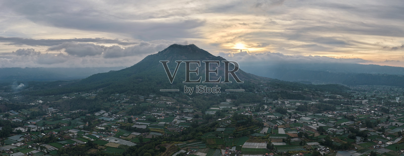 全景式暮光城市景观，山脉火山剪影，城市灯光在阴郁的黄昏氛围中闪耀，巴厘岛金塔马尼照片摄影图片