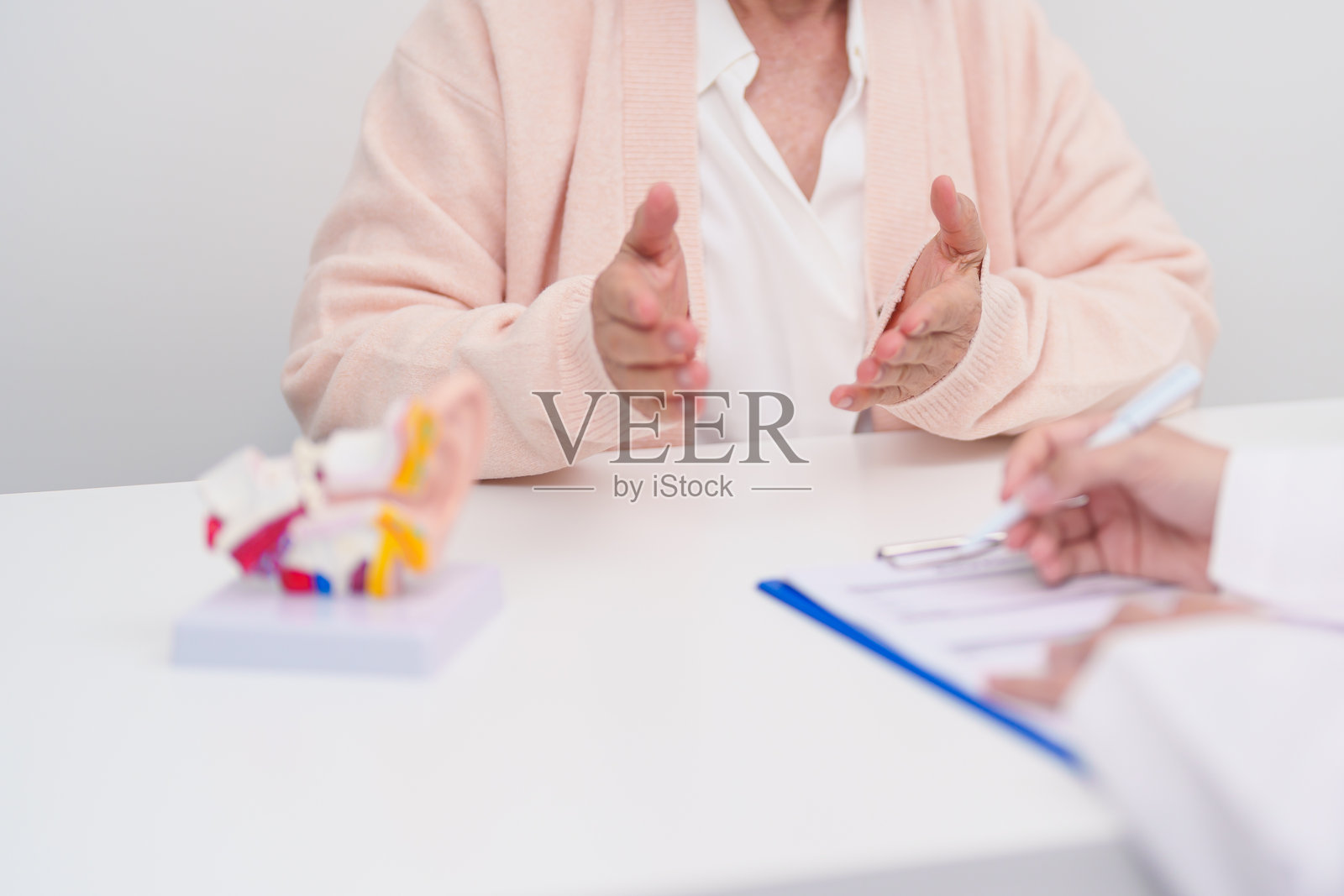 老年患者咨询医生关于耳部疾病。老年人健康医疗诊断。耳部解剖模型，用于说明外耳道闭锁、中耳炎、鼓膜穿孔、梅尼埃病、耳鼻喉科、听力损失。照片摄影图片