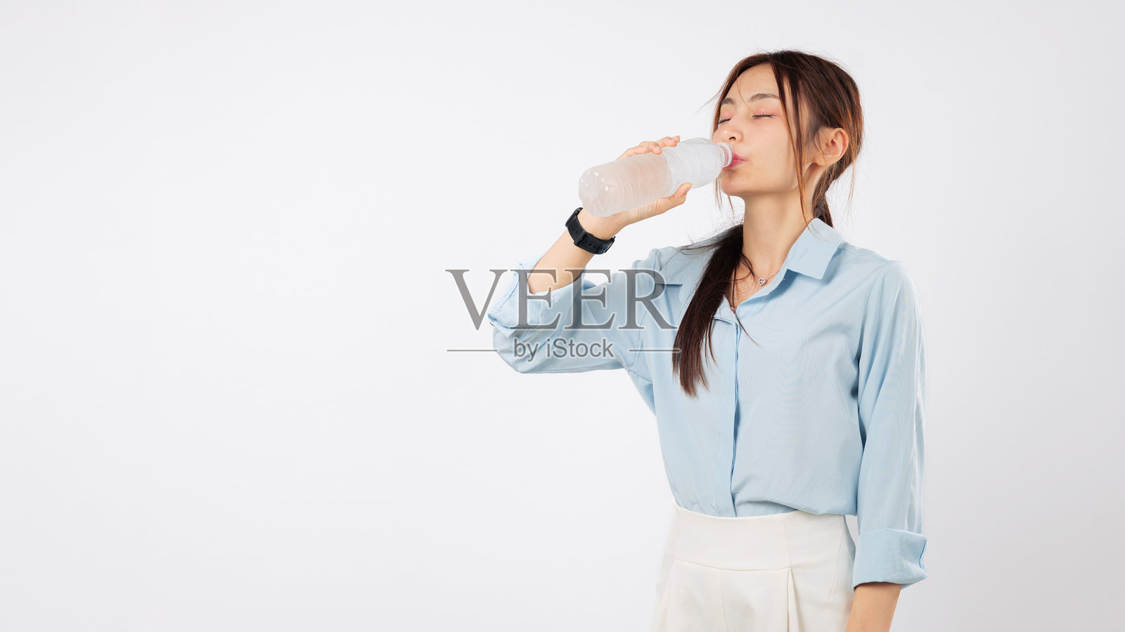 一位年轻迷人的亚洲女性手持一瓶水，享受饮用，闭着双眼。照片摄影图片