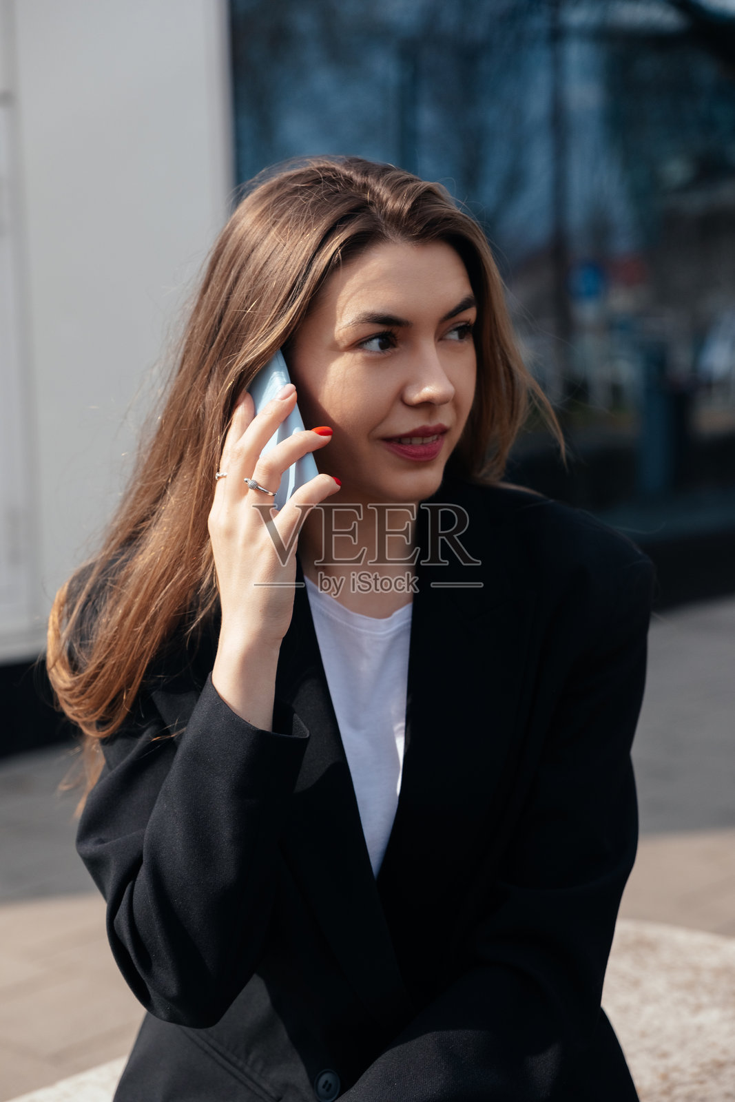 白天，一位年轻女子在城市户外放松的环境中，一边坐着一边进行电话交谈。照片摄影图片