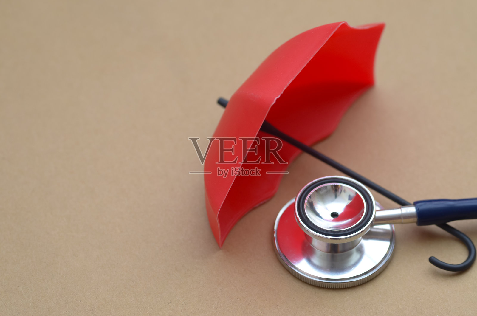 一个红伞下的医疗听诊器，象征着健康保险和医疗计划提供的全面保护和安全。照片摄影图片