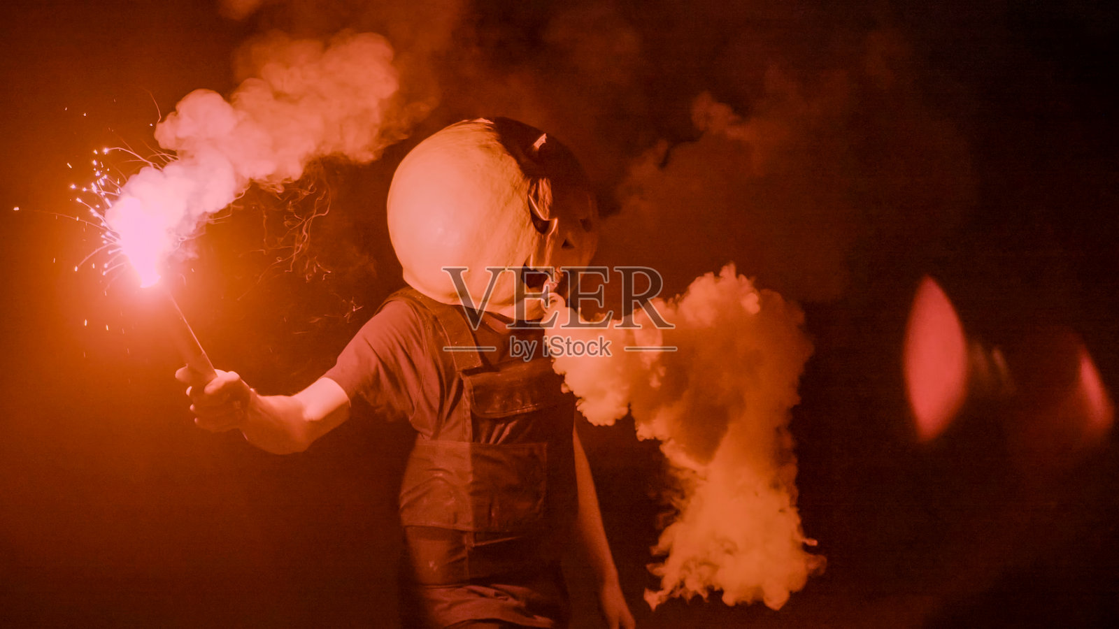 万圣节，一个身穿南瓜或杰克灯笼服装的人，在浓烟和深红色烟花的笼罩下，于漆黑的夜晚现身。照片摄影图片