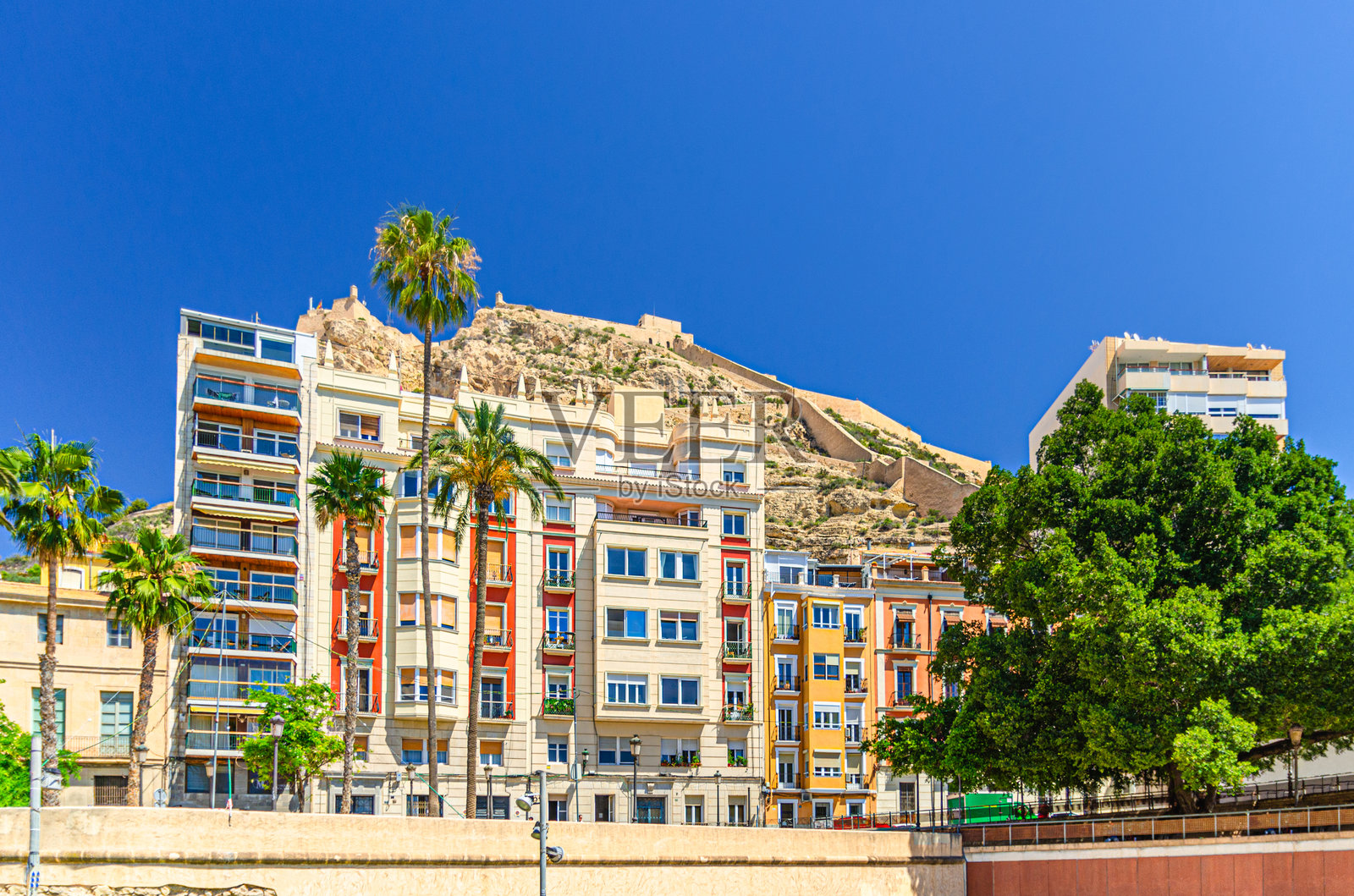 西班牙瓦伦西亚自治区阿利坎特市老城区本纳坎蒂尔山上的圣巴巴拉城堡，阳光明媚的夏日，可以看到色彩缤纷的建筑和棕榈树，这里是阿利坎特市的历史中心。照片摄影图片