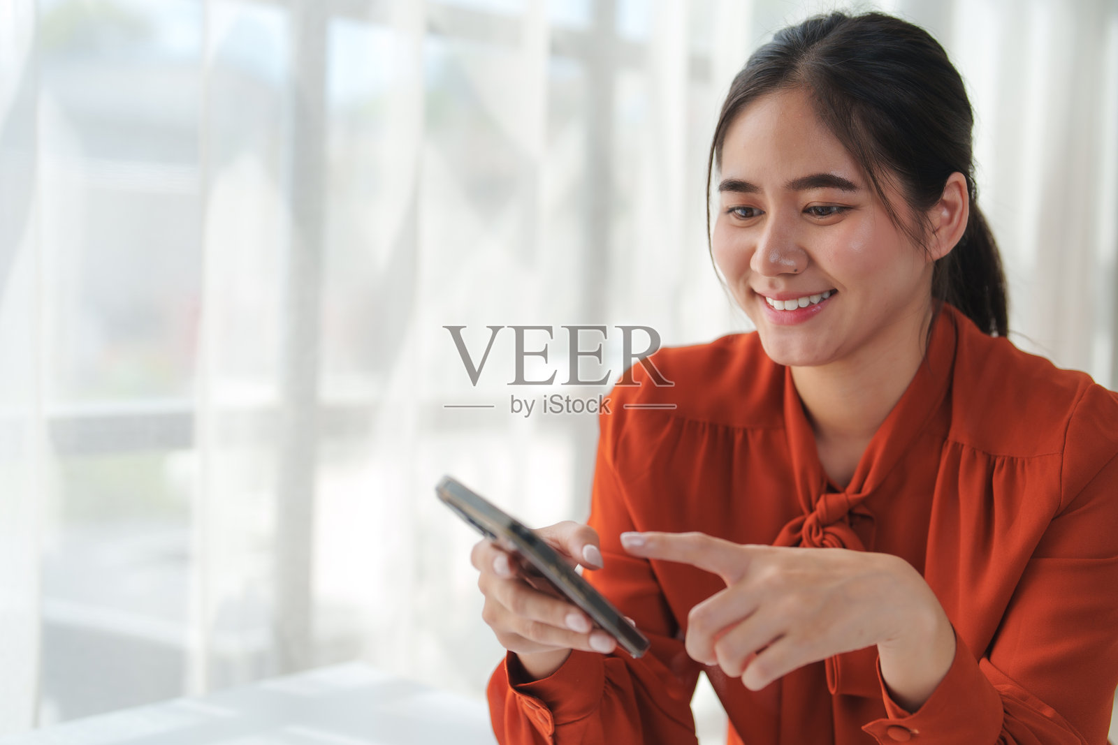 年轻女子在窗边使用智能手机并微笑照片摄影图片